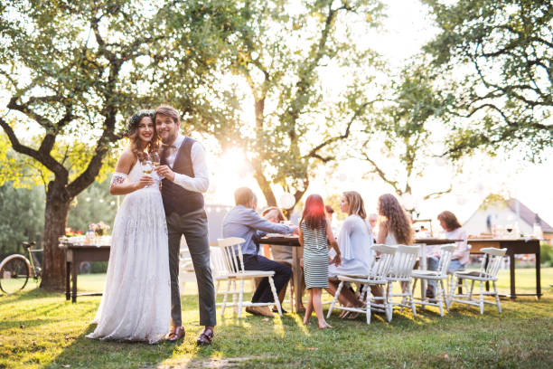 istock Bride and groom clinking glasses at wedding reception outside in the backyard. 985903472