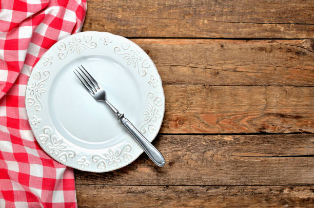 istock White decorative ceramic plate, fork and red checkered tablecloth on left side on old vintage wooden table background - view from above 985903596