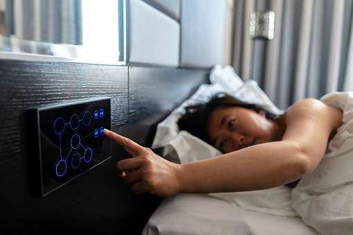 woman sleeping on bed, pushing button to open curtain, in a smart hotel