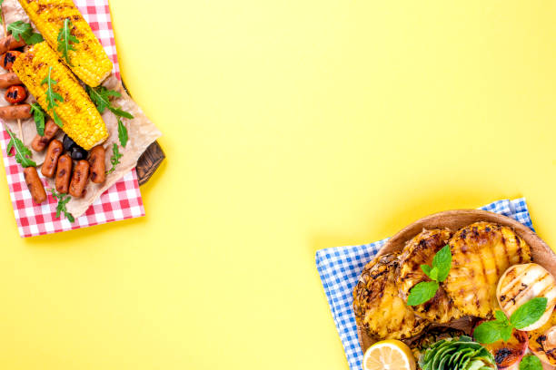 istock Grilled corn and sausages. Yellow background, plastic dishes for a picnic. Free space for text. Copy space. flat lay 985912950