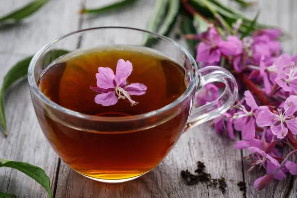 Photo of Traditional Russian herbal drink Ivan-tea in a transparent cup close-up on a wooden table. Positively affects the human body