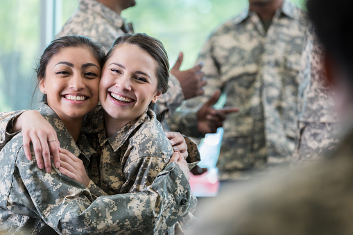 Excited young female soldiers embrace while attending a military academy. They are smiling at the camera.