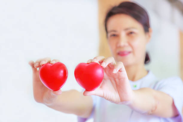 istock Red heart held by smiling female nurse's hand, representing giving effort high quality service mind to patient. Professional, Specialist in white uniform concept 985954392