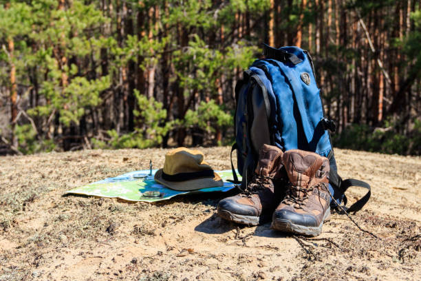 istock Tourist backpack with hiking boots, hat, compass and map on the glade in pine forest 985999218