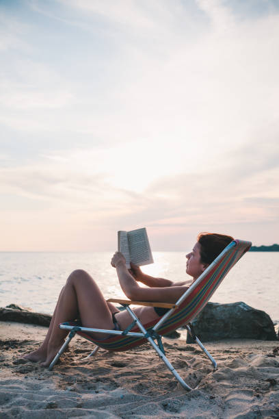 istock Young woman reading a book on the beach 986021080