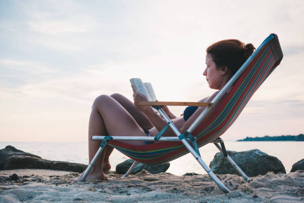 istock Young woman reading a book on the beach 986021084