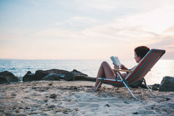 istock Young woman reading a book on the beach 986021092