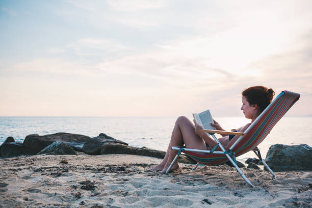 istock Young woman reading a book on the beach 986021116