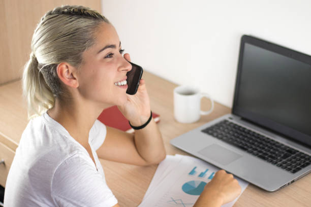 istock Young girl with computer and talking on the phone 986028840