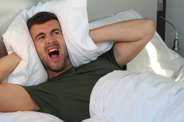 istock Frustrated man covering his ears with pillow 986047102