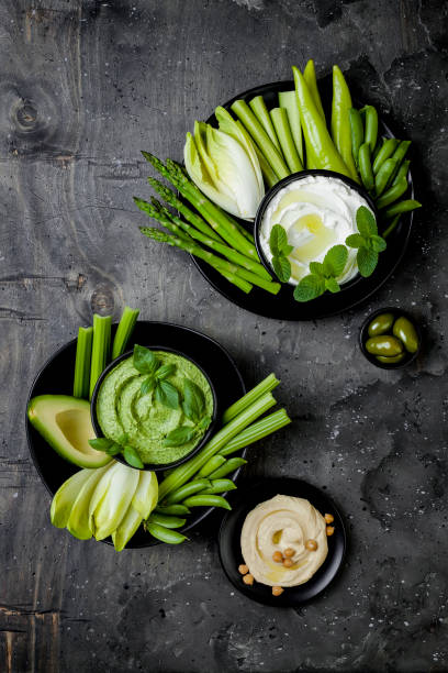 istock Green vegetables snack board with various dips. Yogurt sauce or labneh, hummus, herb hummus or pesto with fresh vegetables. Healthy raw summer platter. 986068852