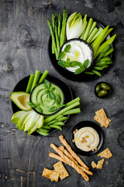 istock Green vegetables snack board with various dips. Yogurt sauce or labneh, hummus, herb hummus or pesto with crackers, grissini bread, fresh vegetables. Healthy raw summer platter. 986069194