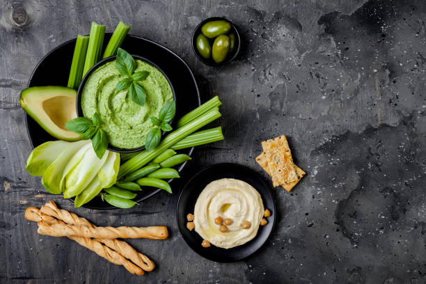 istock Green vegetables snack board with various dips. Yogurt sauce or labneh, hummus, herb hummus or pesto with crackers, grissini bread, fresh vegetables. Healthy raw summer platter. 986069204