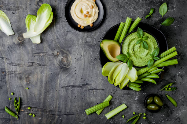 istock Green vegetables snack board with various dips. Hummus, herb hummus or pesto with fresh vegetables. Healthy raw summer vegan platter. Copy space 986069296