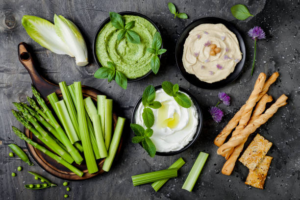 istock Green vegetables snack board with various dips. Yogurt sauce or labneh, hummus, herb hummus or pesto with crackers, grissini bread, fresh vegetables. Healthy raw summer platter. 986069334
