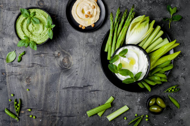istock Green vegetables snack board with various dips. Hummus, herb hummus or pesto with fresh vegetables. Healthy raw summer vegan platter. Copy space 986069350