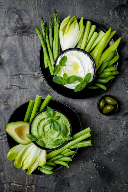 istock Green vegetables snack board with various dips. Yogurt sauce or labneh, hummus, herb hummus or pesto with fresh vegetables. Healthy raw summer platter. 986080928