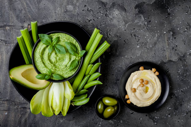 istock Green vegetables snack board with herb hummus or pesto dip. Healthy raw summer appetizer platter. Copy space 986080932