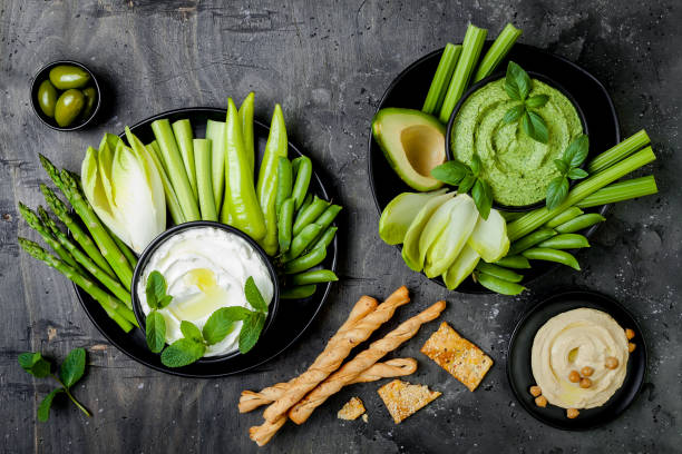 istock Green vegetables snack board with various dips. Yogurt sauce or labneh, hummus, herb hummus or pesto with crackers, grissini bread, fresh vegetables. Healthy raw summer platter. 986080968