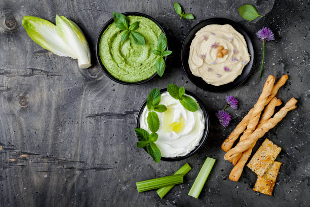 istock Green vegetables raw snack board with various dips. Yogurt sauce or labneh, hummus, herb hummus or pesto with crackers, grissini bread and fresh vegetables. Middle eastern meze snacks set 986081052