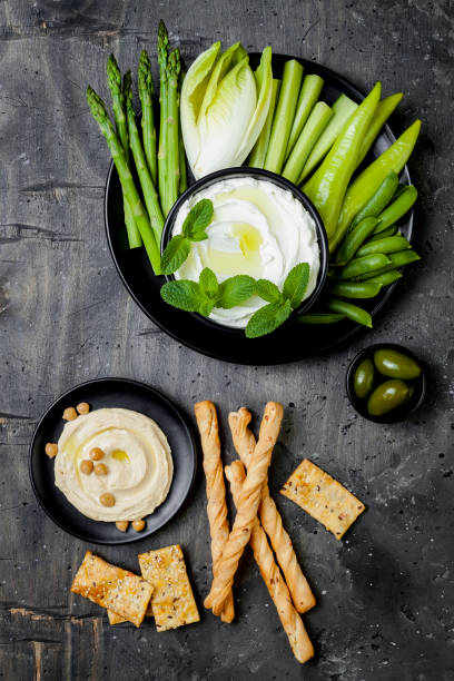 istock Green vegetables snack board with various dips. Yogurt sauce or labneh, hummus with crackers, grissini bread, fresh vegetables. Healthy raw summer platter. 986081070