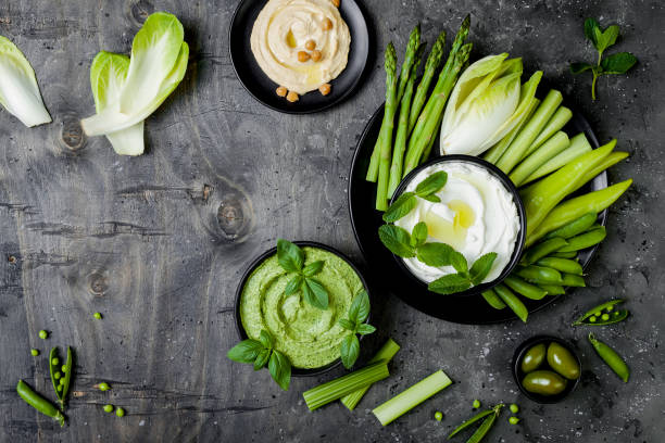 istock Green vegetables snack board with various dips. Yogurt sauce or labneh, hummus, herb hummus or pesto with fresh vegetables. Healthy raw summer platter. 986081082