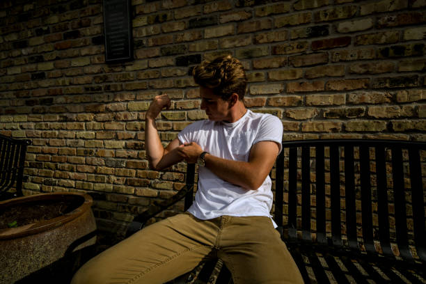 young man sits on city bench flexing - flexing muscles men muscular build t shirt imagens e fotografias de stock