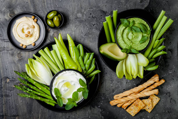 istock Green vegetables snack board with various dips. Yogurt sauce or labneh, hummus, herb hummus or pesto with crackers, grissini bread, fresh vegetables. Healthy raw summer platter. 986091518