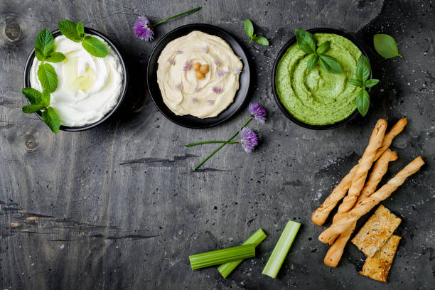 istock Green vegetables raw snack board with various dips. Yogurt sauce or labneh, hummus, herb hummus or pesto with crackers, grissini bread and fresh vegetables. Middle eastern meze snacks set 986091588