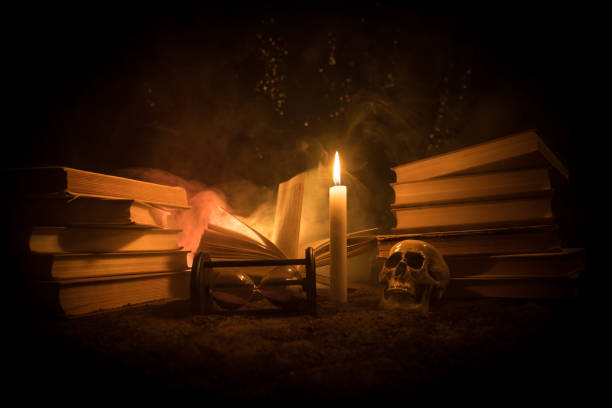 istock Wizard's Desk. A desk lit by candle light. A human skull, old books on sand surface. Halloween still-life background with a different elements on dark toned foggy background. 986107028