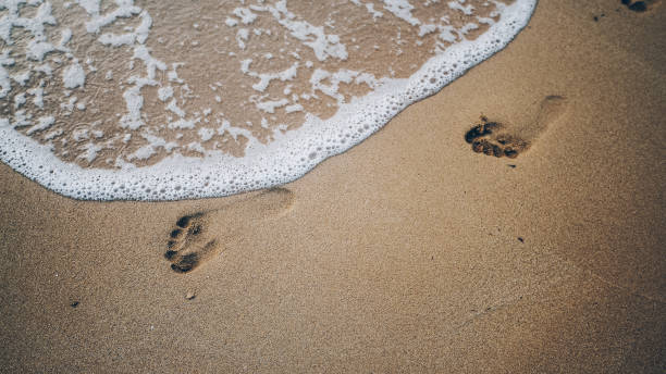 istock Two footprints on sand at the beach with waves and foam 986107080
