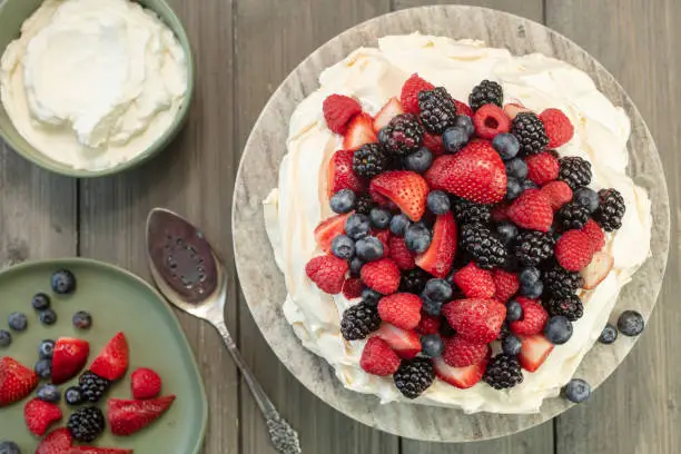 Pavlova meringue cake dessert made with strawberries, blackberries, raspberries and blueberries,  planted on a granite platform