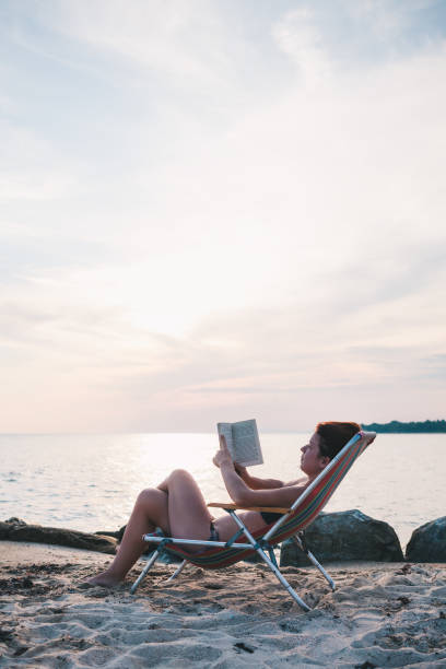 istock Young woman reading a book on the beach 986214258