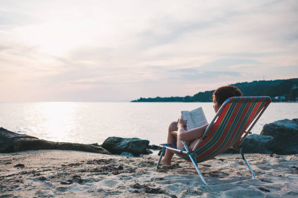 istock Young woman reading a book on the beach 986214266