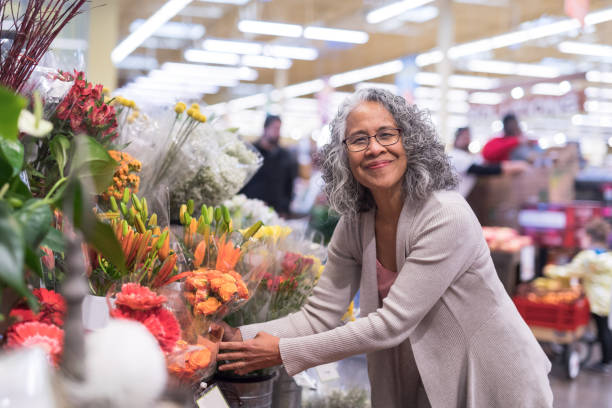 年配の女性が店で花をピックアップします。 - florist supermarket flower bouquet ストックフォトと画像