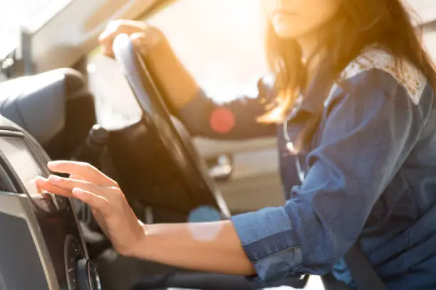 Photo of woman driver hand touching the screen entering an address into the navigation system and turning on car radio system.