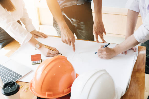 istock Architect Team Brainstorming Planning Design, Civil engineer sketching a blueprint of construction project with small house model and safety helmet in office, Construction Concept. 986342430