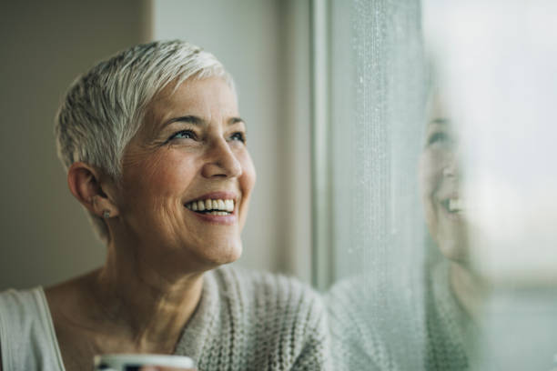 istock Happy mature woman day dreaming while looking through window. 986376340