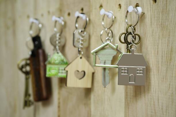 House key with wooden home keyring hanging on wood board background, copy space, property concept stock photo