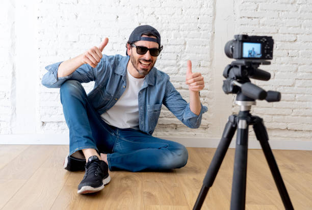 istock young attractive man in casual clothes hat beard hipster style with video camera on tripod against brick wall background in internet blog and blogger concept. 986395942