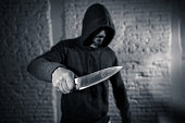 close up of a hands holding a knife of dangerous hooded man standing in the dark in London knife crime concept.