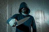 close up of a hands holding a knife of dangerous hooded man standing in the dark in London knife crime concept.