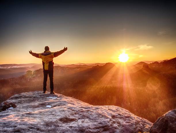 istock Man standing at rocky edge. Young man watching sunrise  at hilly horizon. 986412026