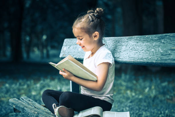 istock little girl is sitting on a bench and is reading a book 986426320