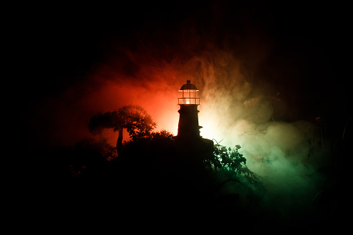 Lighthouse with light beam at night with fog. Old lighthouse standing on mountain. Table decoration. Toned background. Moonlighting. Selective focus