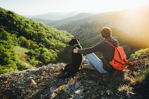 A man sits on a halt during a hike and hugs a black labrador against a beautiful gorge.