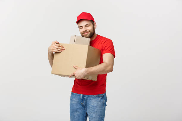 istock Delivery young man in red uniform huging empty cardboard boxes isolated on white background. Copy space for advertisement 986466742
