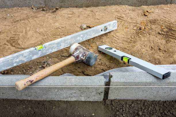 Setting edge restraints with border stones in concrete and level and mallet Setting edge restraints buy putting border curb stones in earth-moist concrete with rubber mallet and bubble level kerbstone stock pictures, royalty-free photos & images