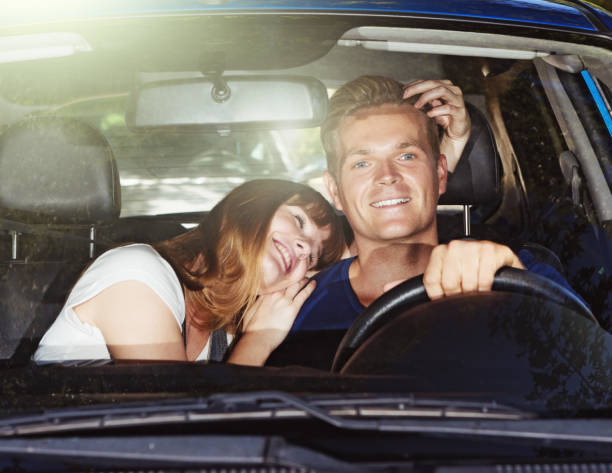 Young woman embraces her driving boyfriend: risky behavior A smiling young man driving a car is distracted by his pretty girlfriend cuddling him. Dangerous behavior! clingy girlfriend stock pictures, royalty-free photos & images