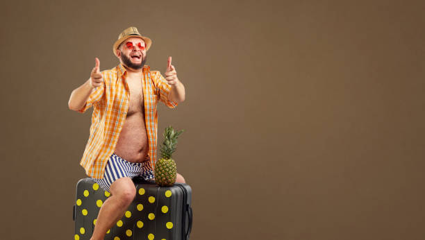 istock A funny overweight man riding a suitcase on a summer vacation 986477338
